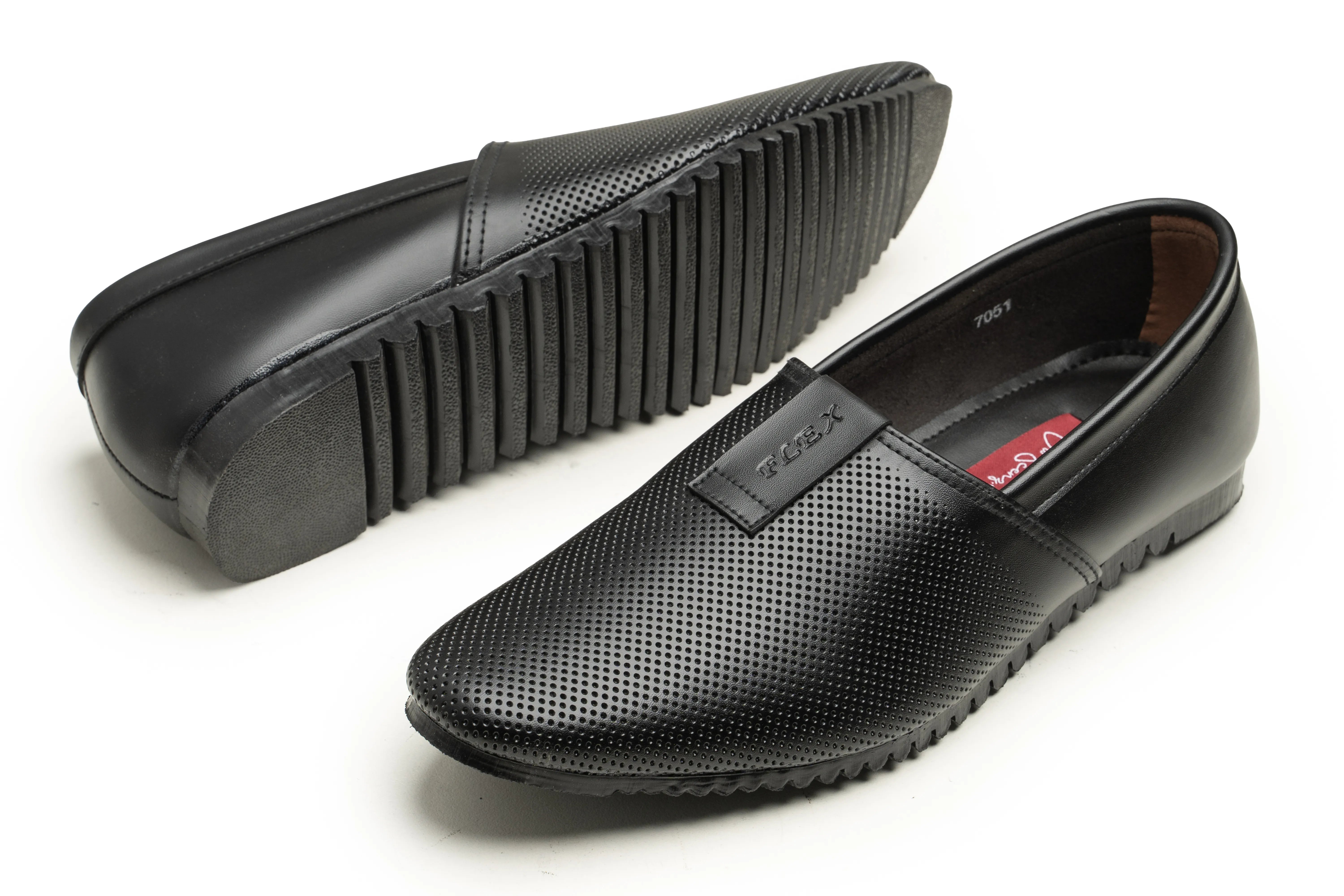 A pair of black slip-on loafers with perforated leather uppers, shown from the side and bottom on a white background. One shoe is turned to display the textured ridged sole, and the other shows the side profile with a small brand tab on the side.