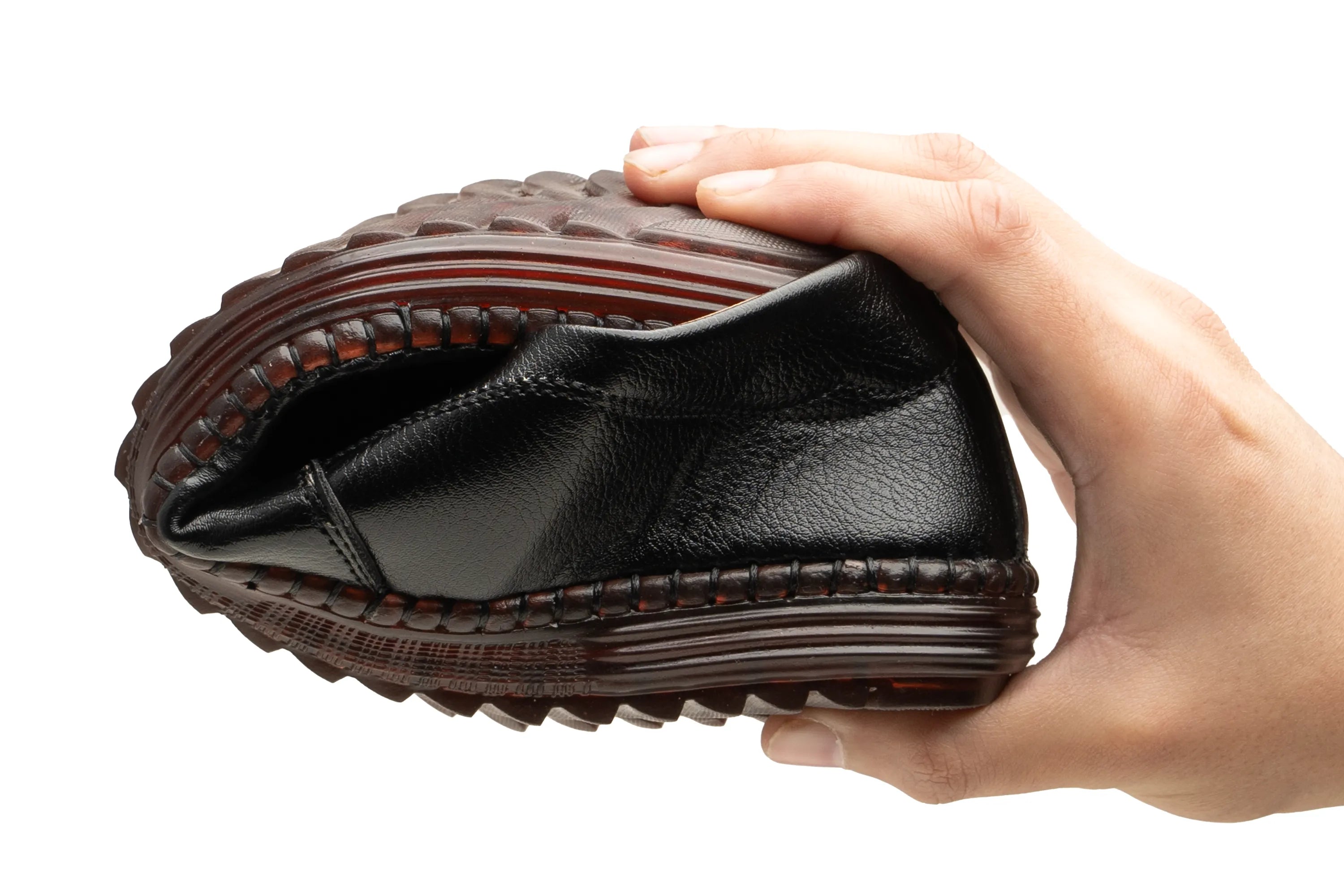 A hand holding a black leather slip-on shoe to show its flexible, squishy sole against a plain white background.